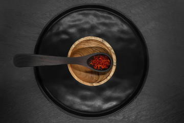Composition of Saffron spices in black wooden spoon and brown wooden bowl