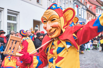 Karnaval - Fastnacht, freundlicher Jeck mit Holzratsche und mit großen Ohren in gelb, rot, blauen Gewand