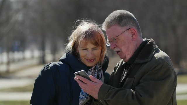elderly couple looking and laughing at a funny picture on the internet on smartphone outdoors