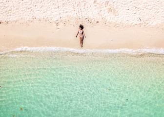 Drone pictures aerial view of a girl on the beach with crystal clear water, a floating boat and boats on a sunny day