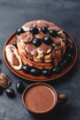 Hot chocolate drink in a cup and pancakes with banana, chocolate sauce and grapes in plate, on dark background