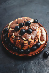 Pancakes with banana, chocolate sauce and grapes in plate, on dark background