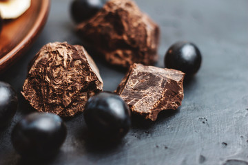 Chunks of dark chocolate and grapes berry on dark background
