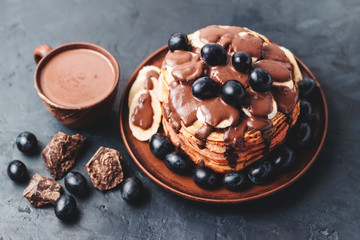 Pancakes with banana, chocolate sauce and grapes in a plate and hot chocolate drink in a cup on dark background