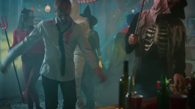 Halloween Costume Party:Group of Young Monsters Dancing, Drinking and Having Fun in Decorated Room with Disco Ball Lights. Zombie, Blood Thirsty Dracula, Mummy, Bewitching Witch and Dazzling She Devil