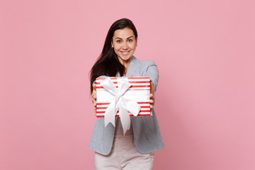 Joyful young woman holding red striped present box with gift ribbon isolated on pink pastel background. St. Valentine's Day, International Women's Day, birthday, holiday concept. Mock up copy space.