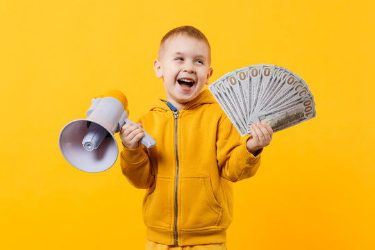 Little happy kid boy in yellow clothes hold fan of money in dollar banknotes, megaphone isolated on orange wall background, children studio portrait. Childhood lifestyle concept. Mock up copy space.