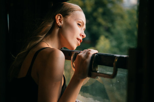 Mood Atmospheric Lifestyle Portrait Of Young Beautiful Blonde Hair Girl Looking Out Of Window From Riding Train. Pretty Teen Enjoying Beauty Of Nature From Moving Train Car In Summer. Travel Concept