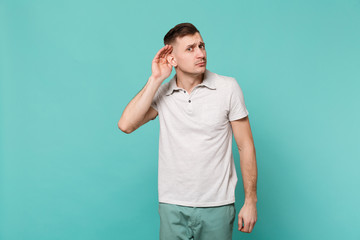 Portrait of curious young man in casual clothes eavesdrop with hearing gesture isolated on blue...