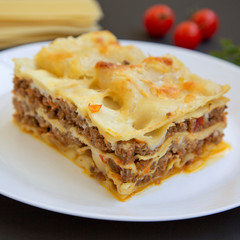 Traditional beef lasagne on a white round plate on black surface, side view. Close-up.