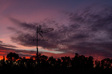 Obraz premium There is a black metallic television antenna and a group of black trees on the beautiful red colorful sunset sky background