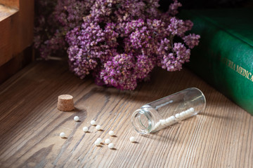 A bottle of homeopathic globules with dried herbs and materia medica