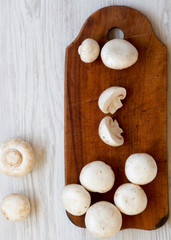 Top view, champignon mushrooms on rustic wooden board over white wooden surface. From above, overhead.