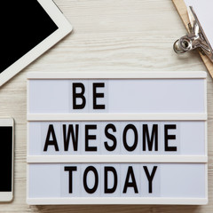 Workspace with tablet, noticepad, sheet and 'Be awesome today' words on modern board over white wooden surface, top view. From above, flat lay.