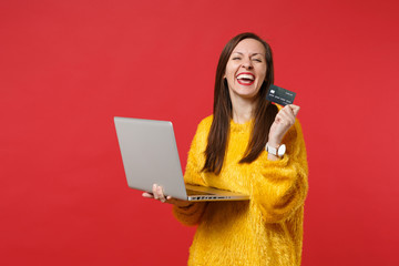 Laughing young woman in yellow fur sweater holding credit bank card laptop pc computer isolated on...