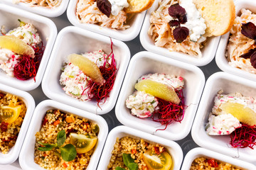 Background of rows of mixed canapes in white square ceramic dishes from above.
