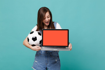 Surprised woman football fan hold soccer ball, laptop pc computer with blank empty screen isolated...