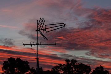 Fototapeta na wymiar There is a black metallic television antenna and a group of black trees on the beautiful red colorful sunset sky background