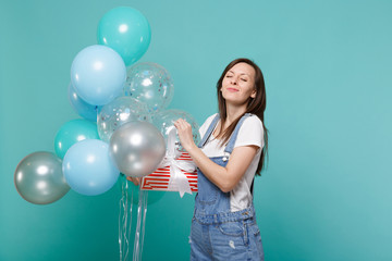 Girl with closed eyes hold red striped present box with gift ribbon celebrating with colorful air...
