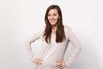 Portrait of smiling pretty young woman in light clothes standing with arms akimbo on waist isolated on white wall background in studio. People sincere emotions, lifestyle concept. Mock up copy space.