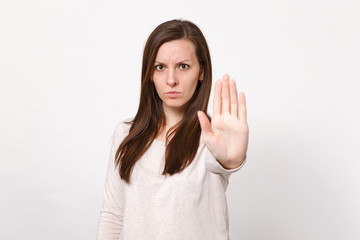 Portrait of serious concerned young woman in light clothes showing stop gesture with palm isolated on white wall background in studio. People sincere emotions, lifestyle concept. Mock up copy space.
