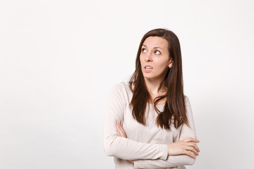 Obraz premium Portrait of puzzled pensive young woman in light clothes looking up, holding hands crossed isolated on white wall background in studio. People sincere emotions, lifestyle concept. Mock up copy space.
