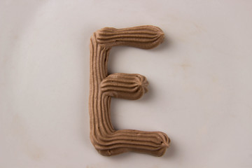 Sweet chocolate letter E drawn with whipped cream on a white plate