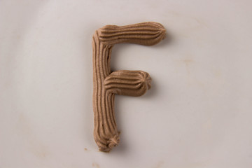 Sweet chocolate letter F drawn with whipped cream on a white plate - 253852475