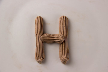 Sweet chocolate letter H drawn with whipped cream on a white plate