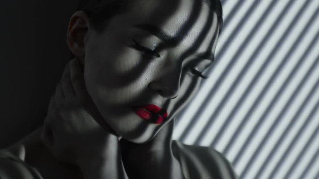 Projection of black and white lines on girl’s face. Close up face of girl with an abstract pattern of lines and red lips on her face. Illumination from the blinds in the room. Concept. Eyes closed.