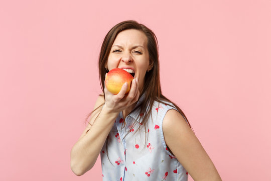 Crazy young woman in summer clothes hold biting fresh ripe red apple fruit isolated on pink pastel wall background, studio portrait. People vivid lifestyle, relax vacation concept. Mock up copy space.