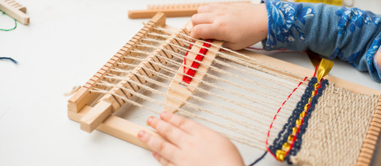 A little girl learns process to weave thick threads. Hands close up.