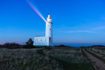 A night long exposure view of the Hurst Point Lighthouse with rainbow beam at blue hour