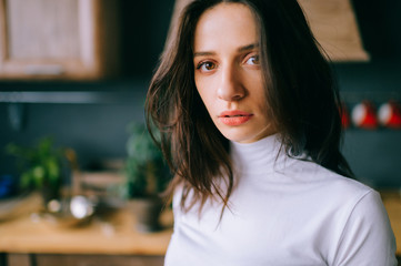 Adorable young model with sensual passionate face, dark long hair posing on kitchen. Indoor lifestyle portrait of cheerful tender amazing girl with spanish appearance and brown eyes looking at camera