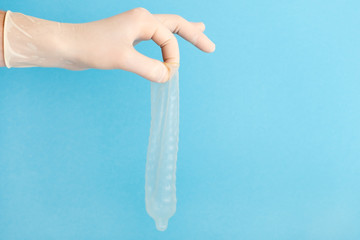 Hand with used condom on blue background