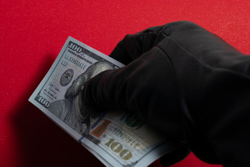 Hand in black glove holding money. Red background. Close Up.