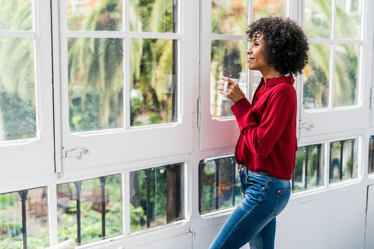Smiling woman with cup of coffee looking out of window at home
