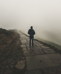 A lone figure stands looking into the fog along a path on the Mam Tor hill in the Peak District, UK