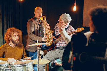 Multicultural band practicing for the gig in home studio. In foreground mixed race singer and in background drummer and saxophonist.
