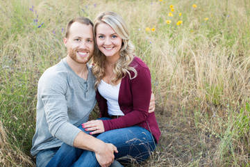 Attractive young couple smiling at camera sitting in wild flowers and grass