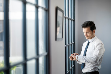 Businessman checking smartwatch in front of large office window