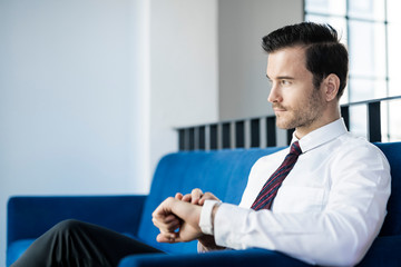 Businessman sitting on blue couch in office checking smartwatch