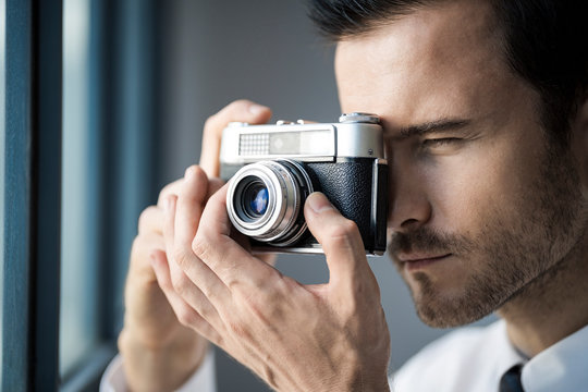 Close-up of businessman taking picture with vintage retro camera in front of office window