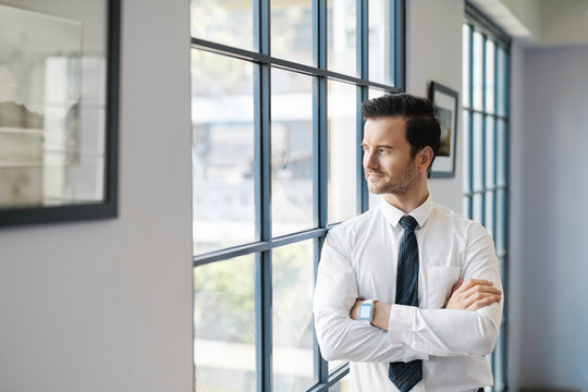 Confident businessman standing in office looking out of window