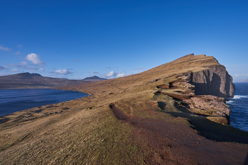 Wild coast and high cliffs on Faroe island Vagar during the sunny spring day. Faroe islands, part of Danish kingdom in nord atlantic, beautiful example of wild scandinavian countryside without trees.