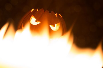 Spooky smiling halloween pumpkin in hot burning hell fire flames. The big helloween symbol has a mad face glowing eyes and also a glow in its mouth and teeth. Black orange nightmare of October 31st