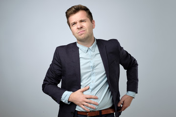 European young man in suit having stomach pain. Colic or flatulence - obrazy, fototapety, plakaty