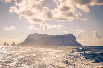The Faraglioni of Capri island silhouette behind the wake of a boat, Italy