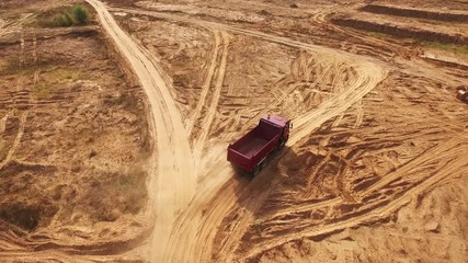Aerial view of the empty large red truck moving on a sandy track for the sand in desert or dunes. Beautiful view from above.