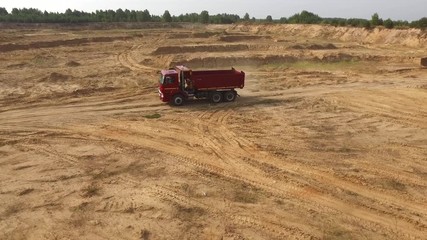 Close-up view the red truck moving on desert or dune track against grey sky and trees on the background. Beautiful view from above.